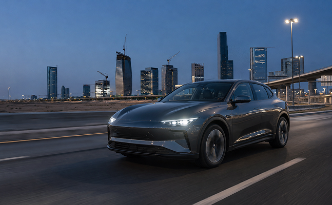 Dark grey electric SUV on a road at dusk with a city skyline behind